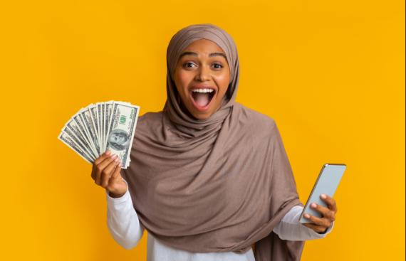 Girl in a hijab holding money in one hand and a phone in the other