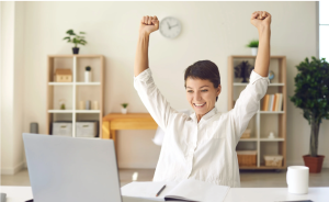 Woman sitting on a table looking at a computer and celebrating