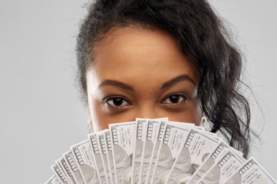 brown woman holding 100 dollar bill close to her face