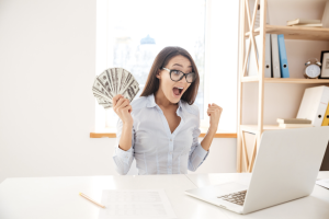 Girl excited in front of a laptop holding money 