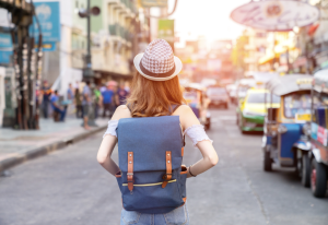 Woman walking away carrying a book bag and wearing a hat 